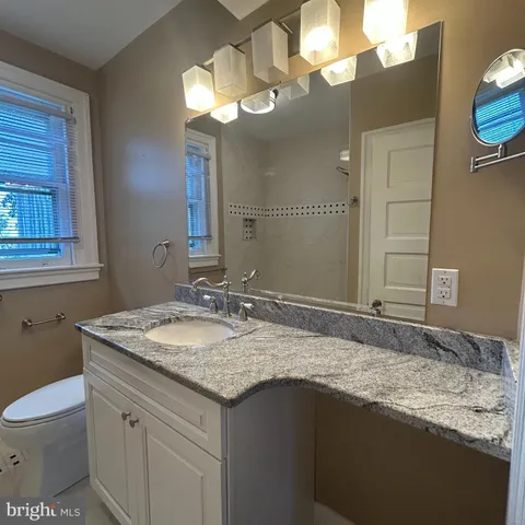 a bathroom with a granite countertop sink a toilet and a mirror