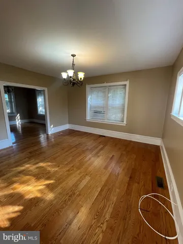 an empty room with chandelier fan and wooden floor