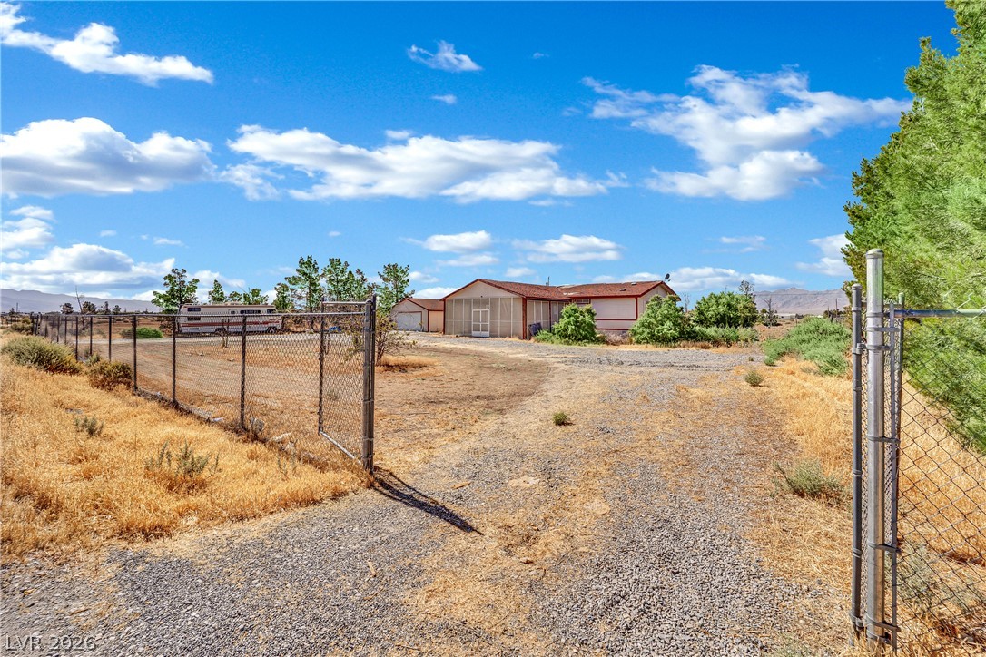 4361 Maple Road Pahrump, NV 89048 - Photo 38 of 46 A long gravel driveway leads to a modest home with a fenced perimeter and mountain views.