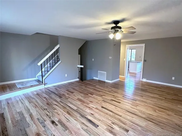 a view of an empty room with wooden floor and a ceiling fan