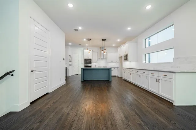 a living room with stainless steel appliances kitchen island wooden floors and white walls
