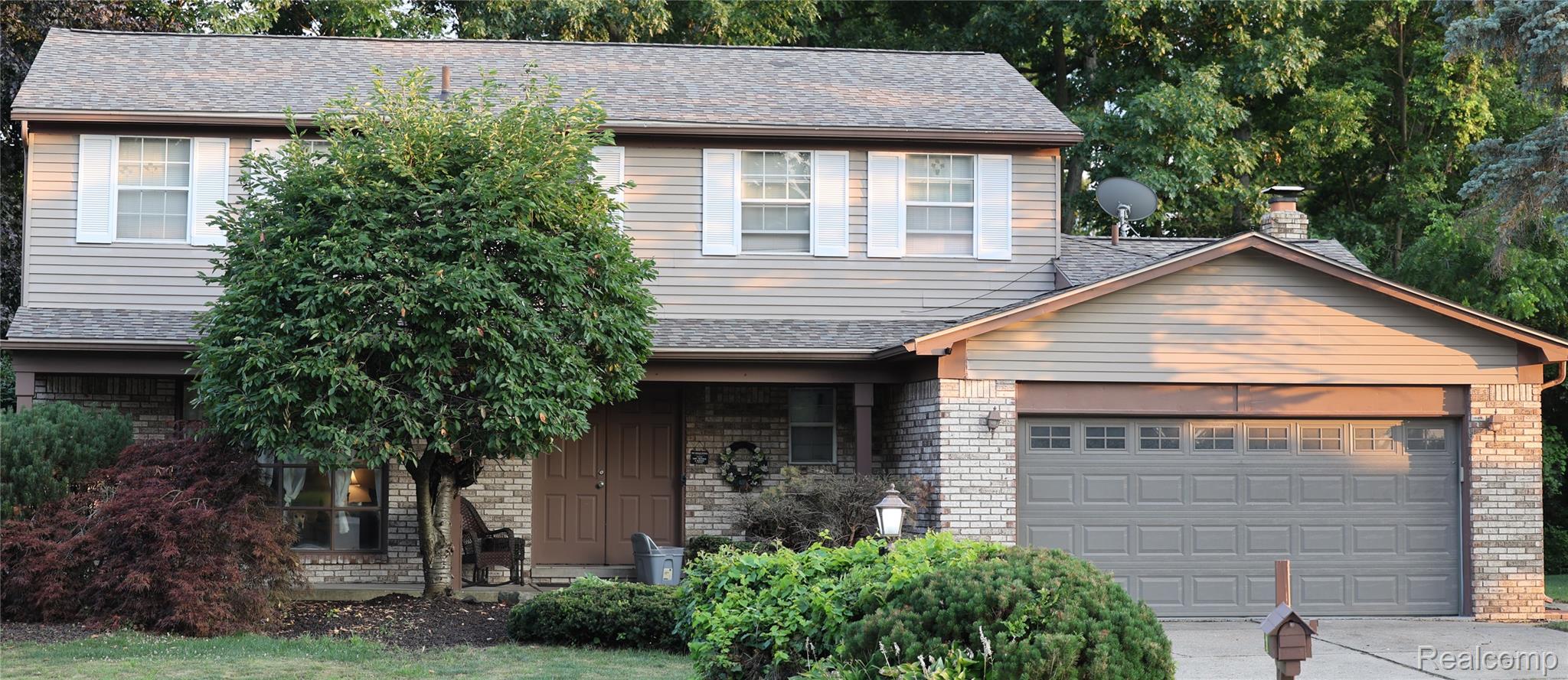 Two-story residence featuring a combination of brick and siding exterior, an attached garage with a panel door, and mature landscaping