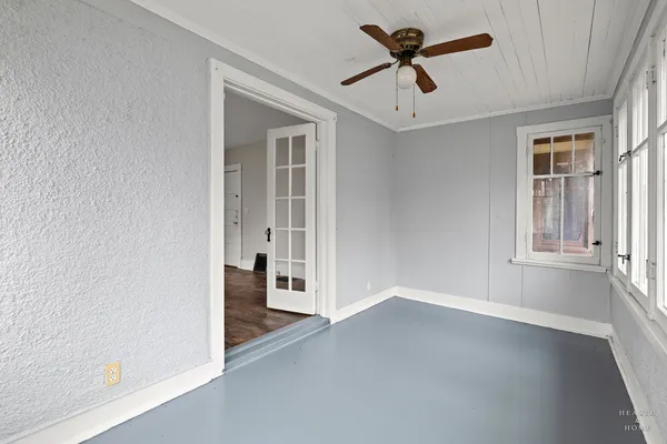 an empty room with chandelier fan and windows