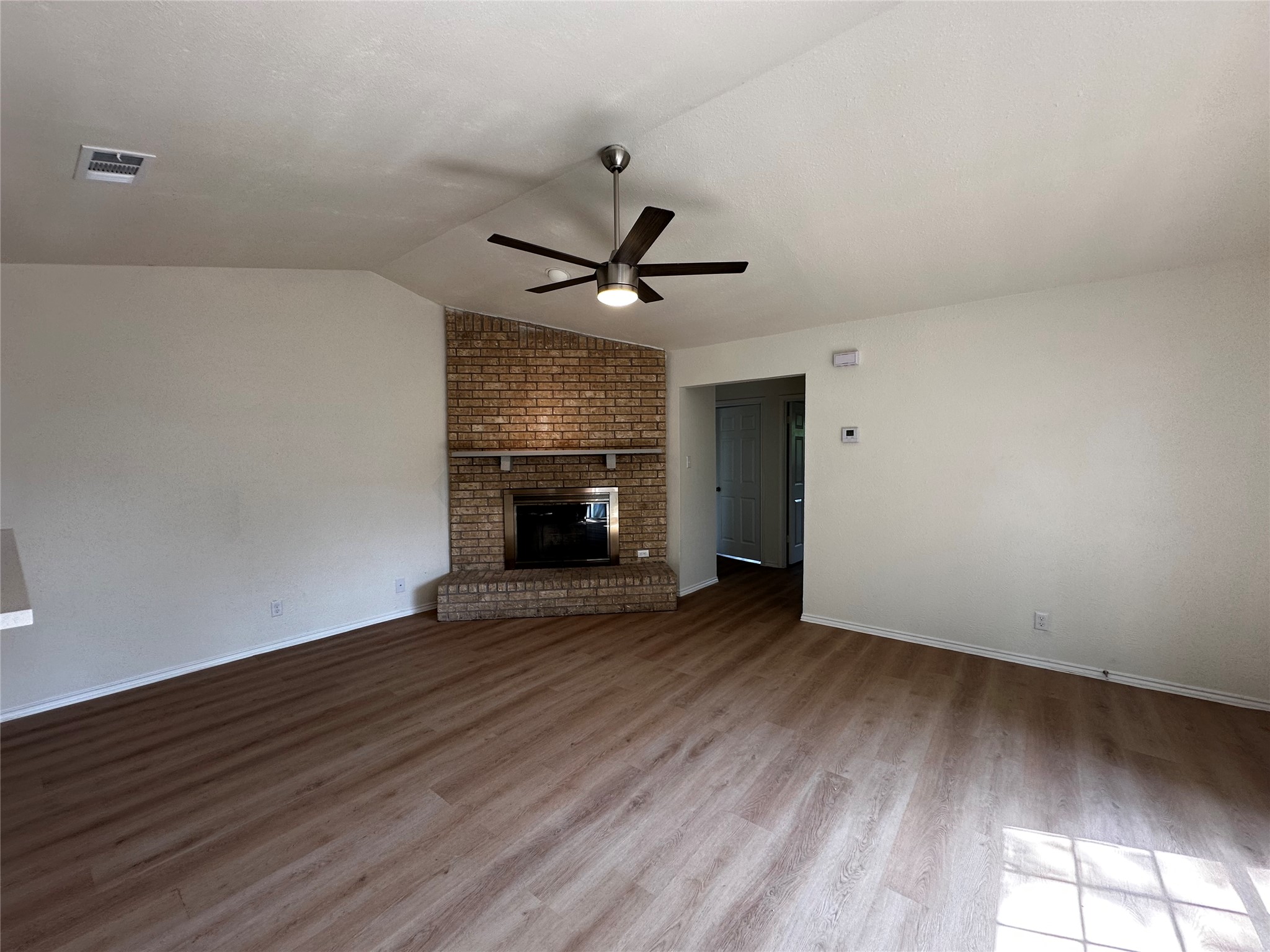 8809 Cainwood Lane Austin, TX 78729 - Photo 10 of 27 an empty room with wooden floor a ceiling fan and a fireplace
