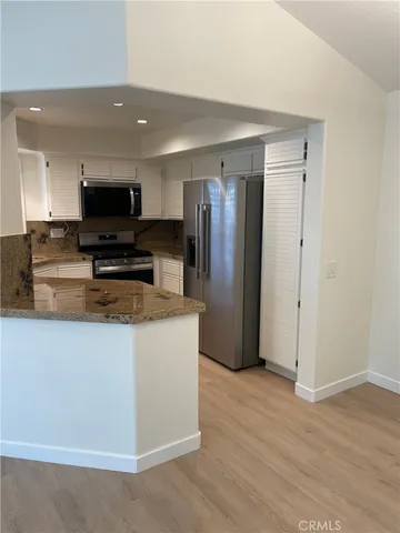 a view of kitchen with stainless steel appliances wooden floor and living room