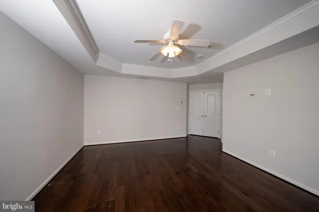 a view of an empty room with wooden floor and a fan