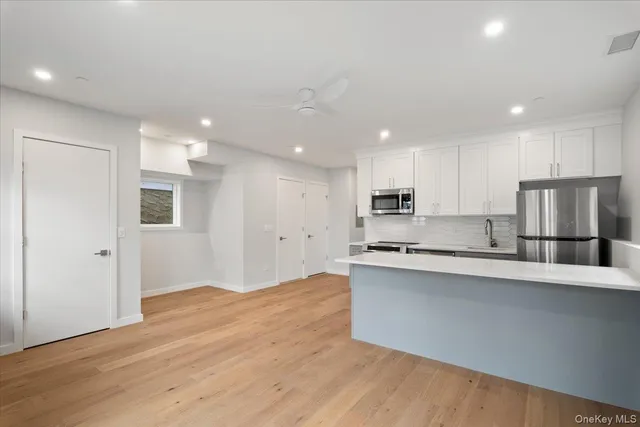 a large kitchen with stainless steel appliances granite countertop a stove a refrigerator a sink a microwave and white cabinets with wooden floor