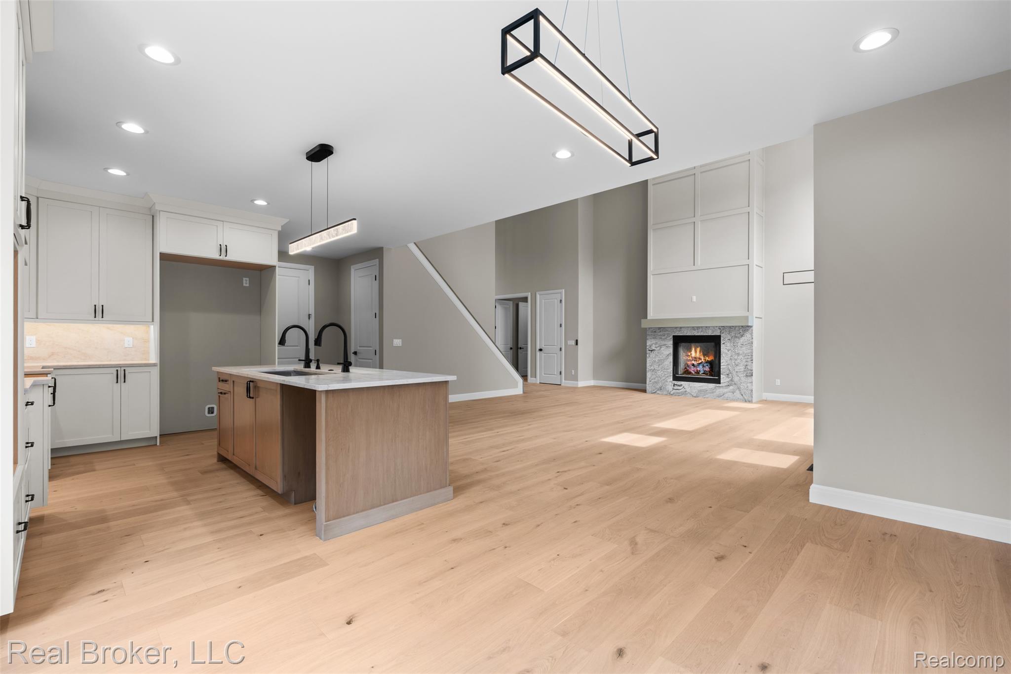 12114 22 Mile Road Utica, MI 48315 - Photo 23 of 70 Open-concept living space with light wood-finish flooring, a contemporary fireplace with a stone surround, and an island kitchen featuring a double sink