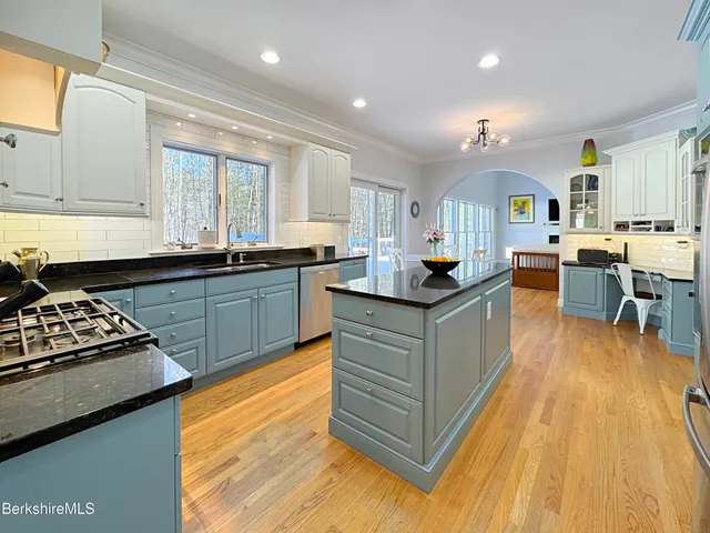 a kitchen with stainless steel appliances granite countertop a stove top oven a sink dishwasher and white cabinets with wooden floor