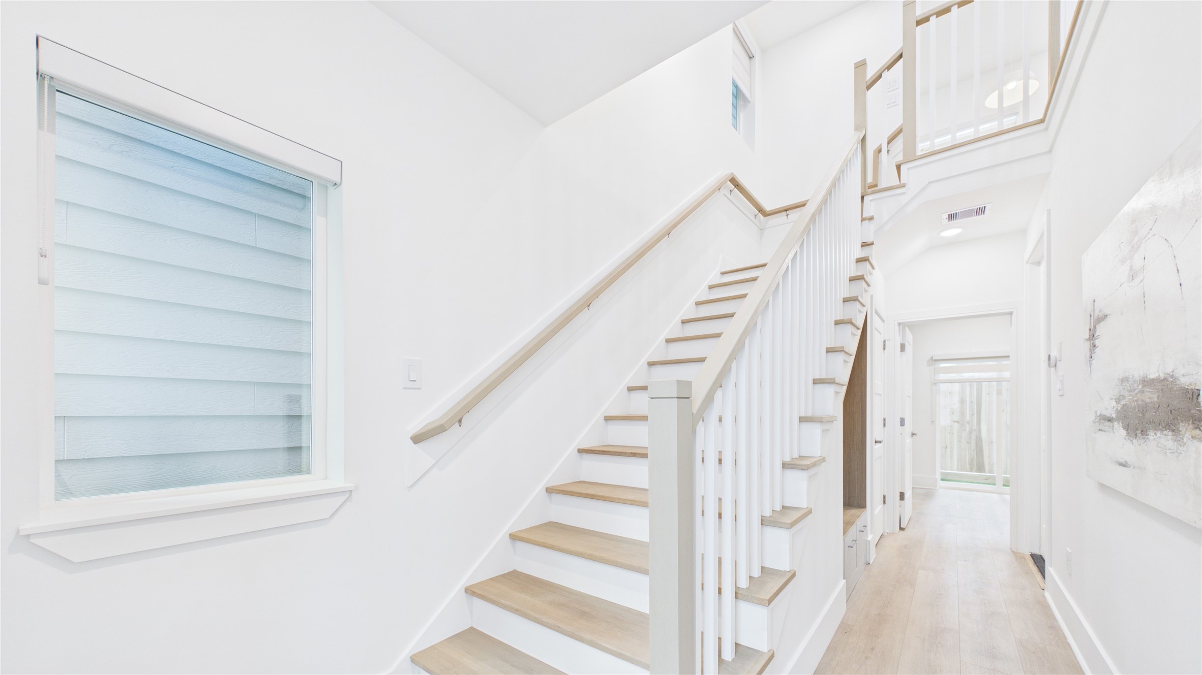 602 Skyland Terrace Way Houston, TX 77009 - Photo 4 of 40 This photo showcases a bright, modern entryway with a wooden staircase featuring white railings. It has sleek hardwood floors, a large window, and a hallway leading to a glass door, creating an open and inviting atmosphere.