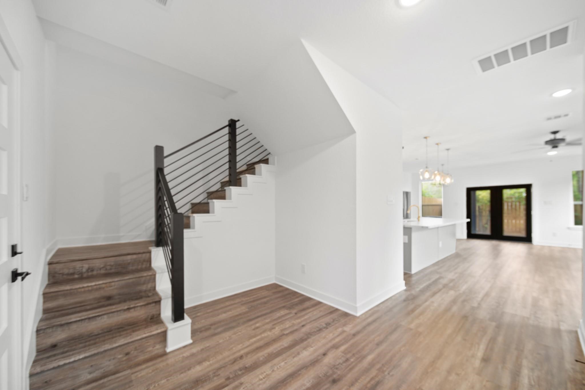 5813 England Street, Unit A Houston, TX 77021 - Photo 9 of 18 Bright, open-concept living area featuring stylish wood flooring, modern staircase with sleek railing, and a spacious kitchen with elegant lighting.