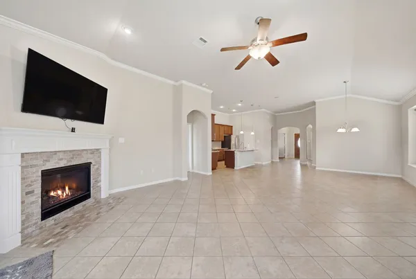 a view of a livingroom with a fireplace a ceiling fan and a kitchen view