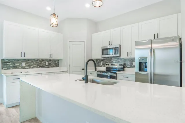 a kitchen with stainless steel appliances granite countertop a refrigerator a sink a stove and white cabinets