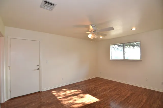 an empty room with wooden floor and fan