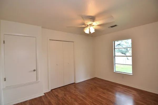 an empty room with wooden floor fan and windows