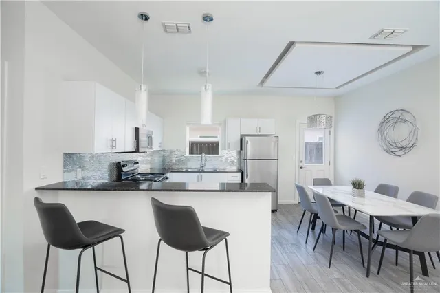 a kitchen with stainless steel appliances kitchen island granite countertop a dining table chairs and a refrigerator