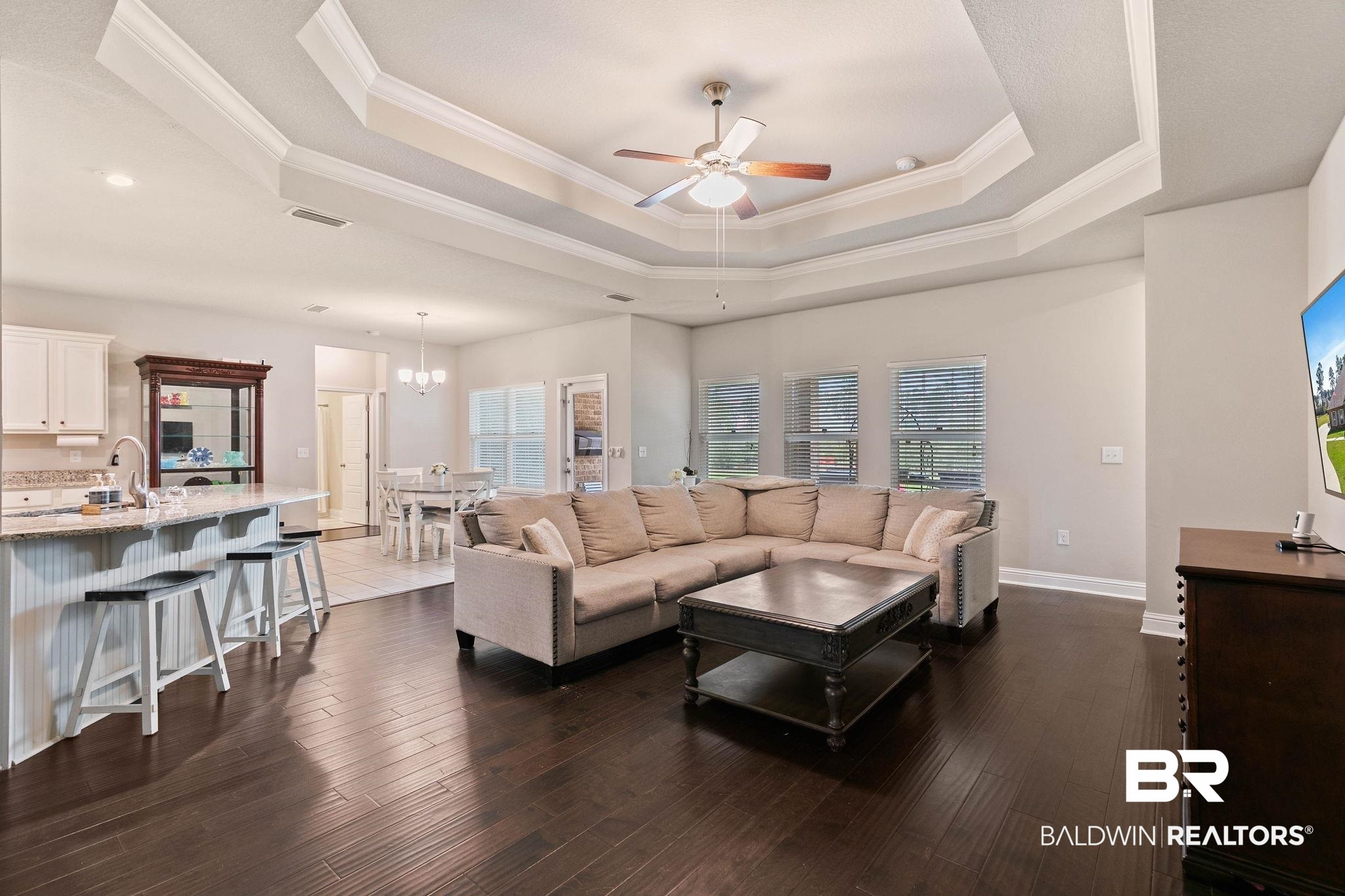 12750 B Jenkins Pit Road Daphne, AL 36527 - Photo 14 of 89 Living room featuring a ceiling fan, crown molding, dark wood finished floors, suspended lighting, and a tray ceiling