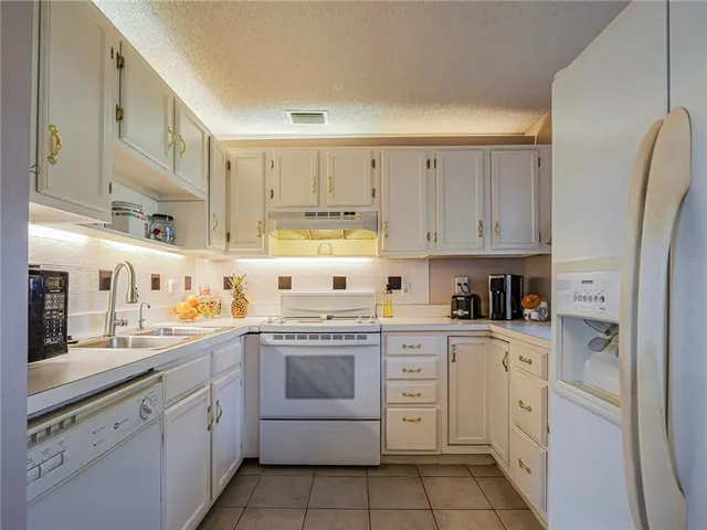 a kitchen with stainless steel appliances granite countertop white cabinets sink and white appliances