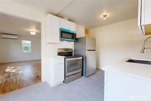 a kitchen with stainless steel appliances a stove a microwave a refrigerator a sink and white cabinets with wooden floor