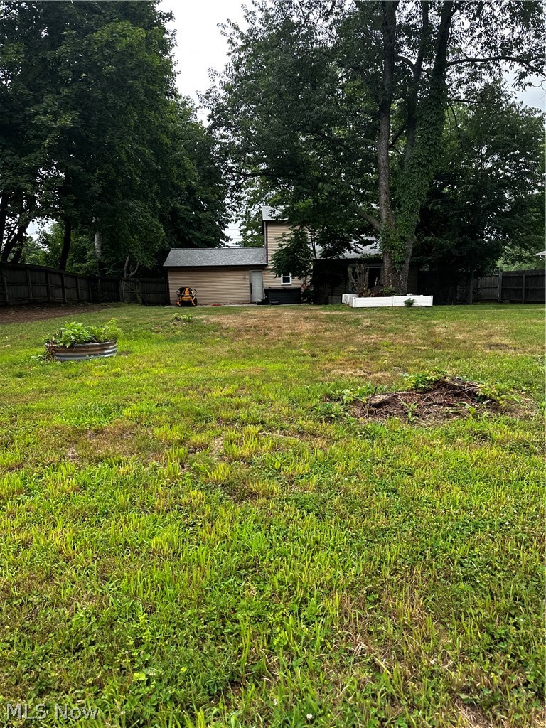 198 Park Road Painesville, OH 44077 - Photo 28 of 31 Expansive green space featuring a detached auxiliary building with a shingled roof, a large mature tree, a privacy fence, and a raised planter bed