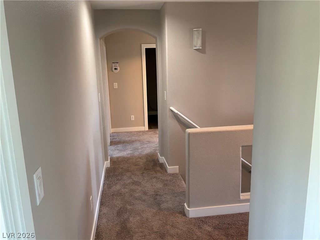 9041 Rendon Street Las Vegas, NV 89143 - Photo 23 of 34 An arched doorway and wall sconce lighting detail this upper-level hallway with carpeted flooring.