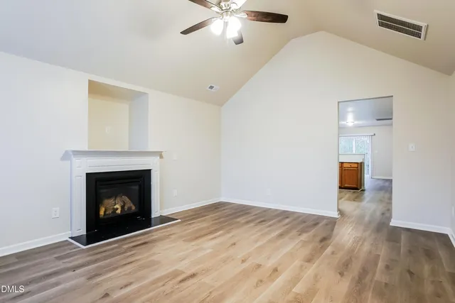 a view of an empty room with wooden floor fireplace and a window