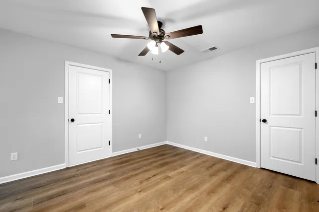 an empty room with wooden floor ceiling fan and windows