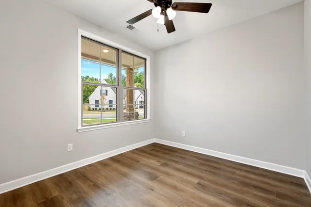 an empty room with wooden floor fan and windows