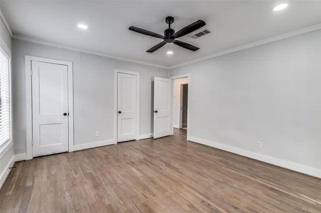 a view of an empty room with wooden floor and a ceiling fan
