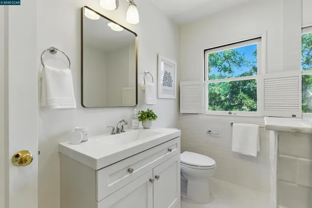 a bathroom with a toilet a sink a mirror a window and vanity