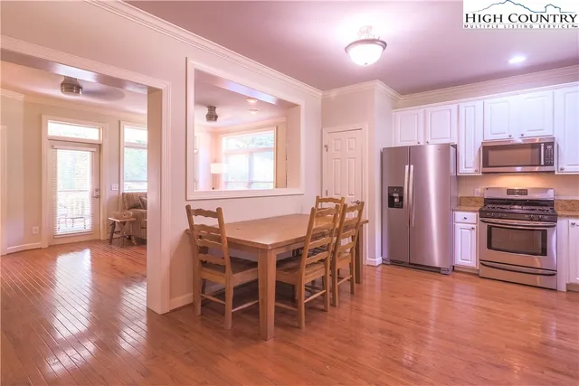 a kitchen with stainless steel appliances a refrigerator a stove a dining table and chairs with wooden floor