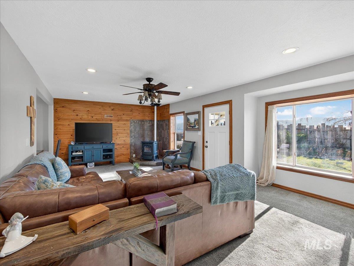 2588 West Sales Yard Road Emmett, ID 83617 - Photo 15 of 49 Living room featuring wooden walls, a wood stove, carpet floors, an accent wall, and ceiling fan