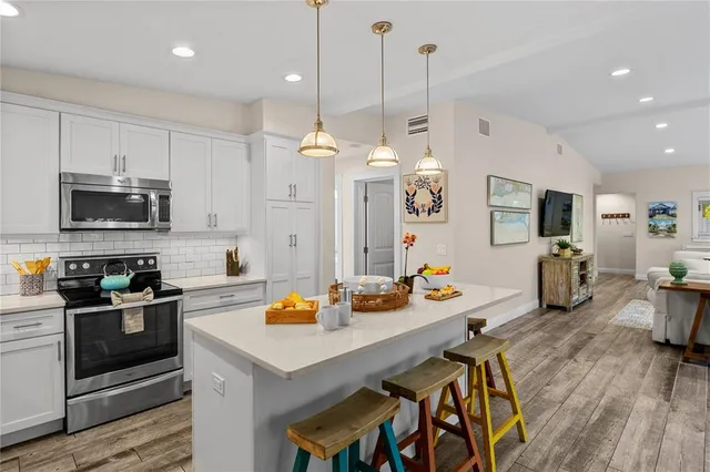 a open kitchen with stainless steel appliances granite countertop a stove a sink dishwasher a dining table and chairs with wooden floor