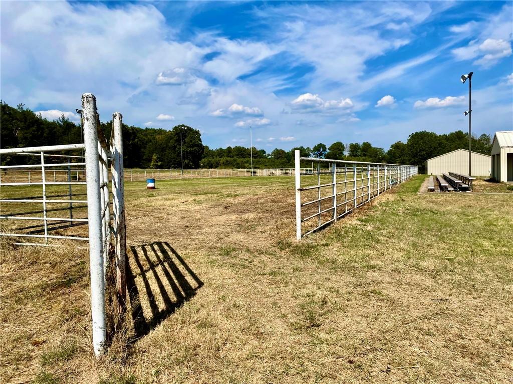 8524 Youth Ranch Road Mulberry, AR 72947 - Photo 25 of 40 Expansive fenced field featuring a metal gate entrance, perimeter fencing, a utility building, bleacher seating, and tall exterior lighting