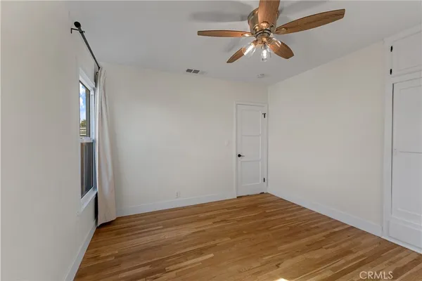 a view of empty room with wooden floor and fan