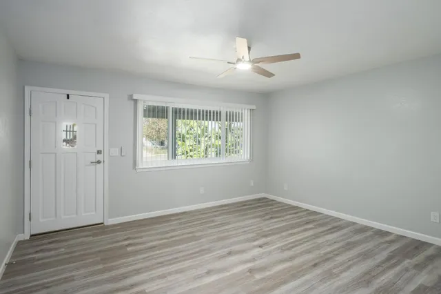an empty room with wooden floor chandelier fan and windows