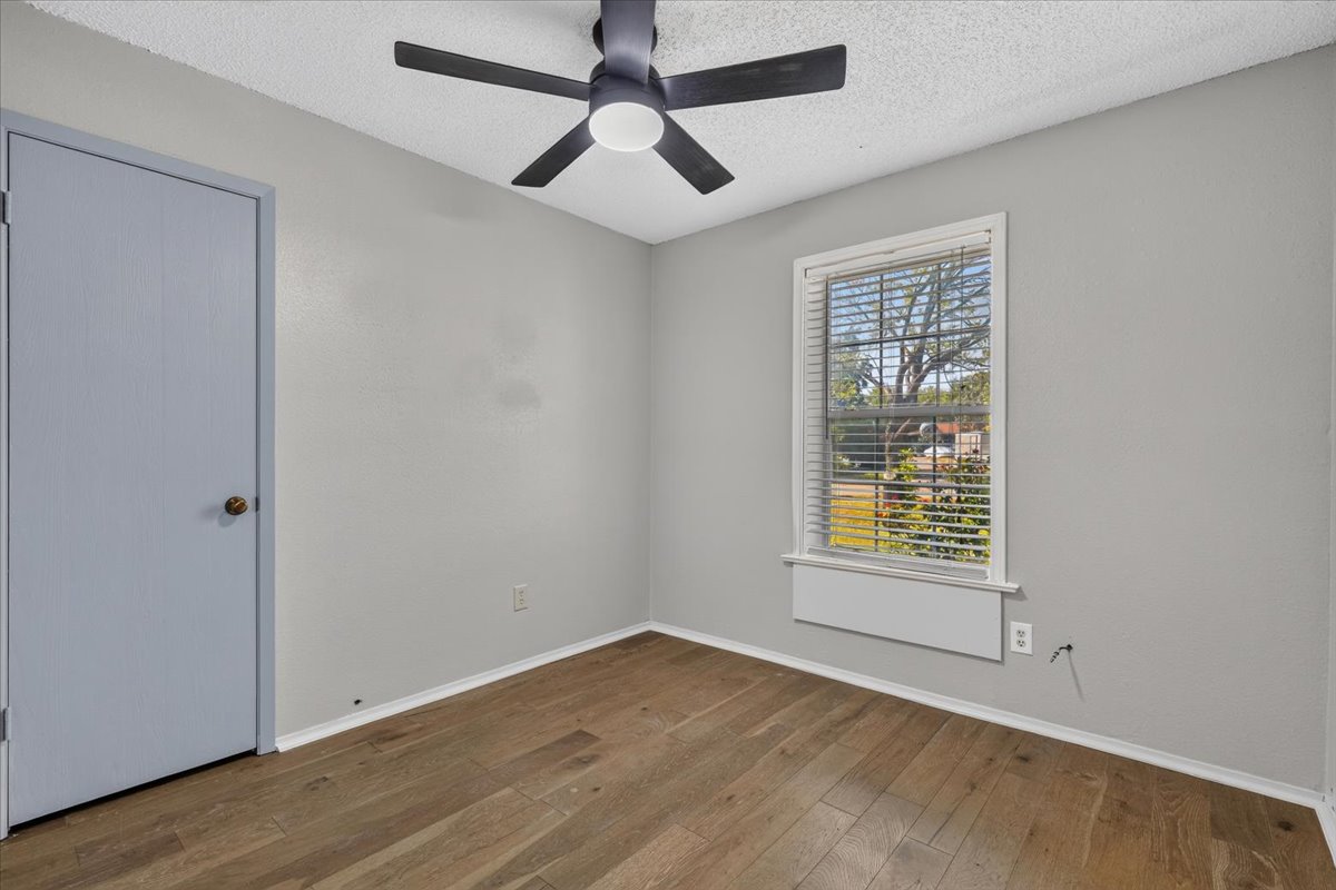 6200 Shadow Bend Austin, TX 78745 - Photo 23 of 33 A well-lit bedroom with modern wood-look flooring, a window providing outdoor views, and a stylish ceiling fan.