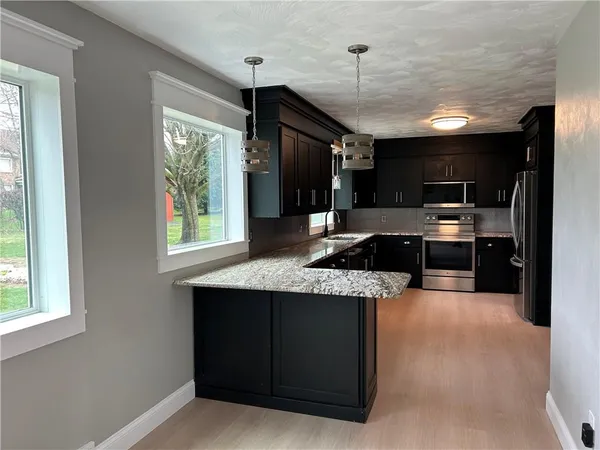 a kitchen with granite countertop a sink stainless steel appliances wooden floor and a window