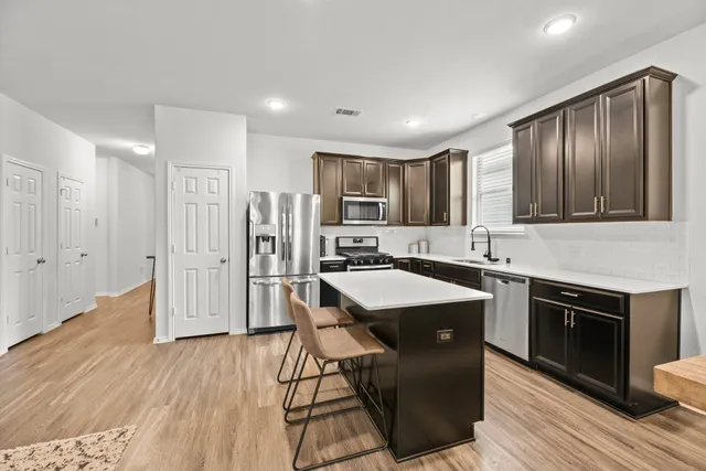 a kitchen with stainless steel appliances granite countertop a refrigerator a sink dishwasher a stove and white countertops with wooden floor