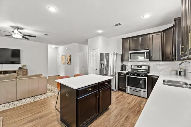 a kitchen with stainless steel appliances granite countertop a stove top oven a sink dishwasher a refrigerator and a microwave oven with wooden floor
