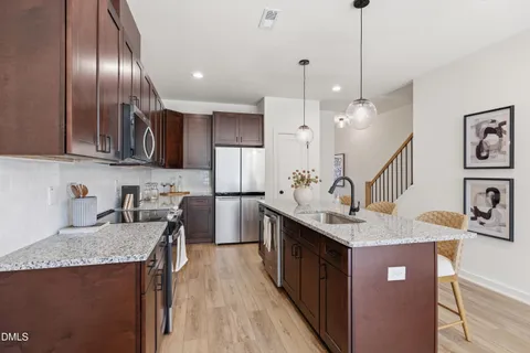 a open kitchen with stainless steel appliances granite countertop a sink dishwasher and a dining table with wooden floor