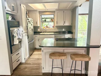 a kitchen with stainless steel appliances kitchen island granite countertop a refrigerator a stove a sink and white cabinets with wooden floor