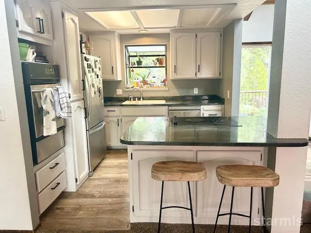 a kitchen with stainless steel appliances kitchen island granite countertop a refrigerator a stove a sink and white cabinets with wooden floor