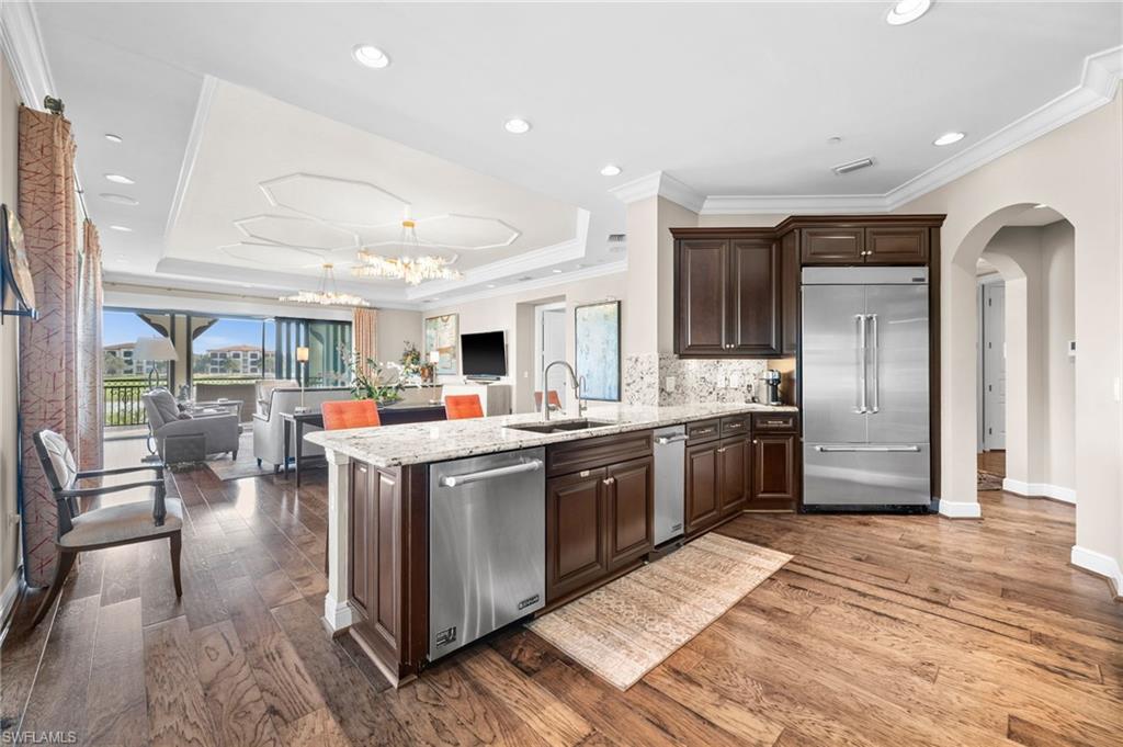 16436 Carrara Way, Unit 102 Naples, FL 34110 - Photo 14 of 43 Kitchen with dark brown cabinets, arched walkways, appliances with stainless steel finishes, light stone counters, and a peninsula