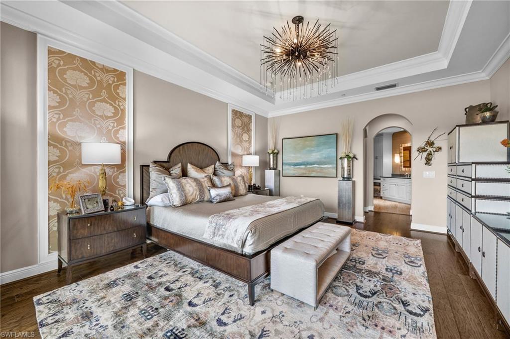 16436 Carrara Way, Unit 102 Naples, FL 34110 - Photo 17 of 43 Bedroom featuring arched walkways, dark wood finished floors, crown molding, a tray ceiling, and a chandelier