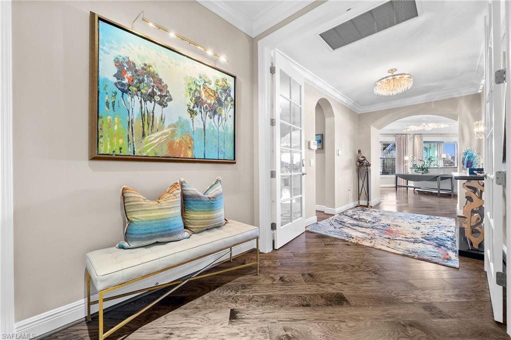 16436 Carrara Way, Unit 102 Naples, FL 34110 - Photo 5 of 43 Entrance foyer with arched walkways, crown molding, dark wood-style flooring, and a chandelier