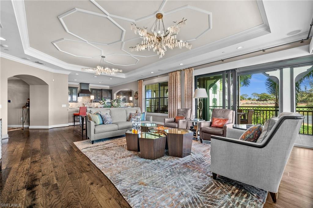 16436 Carrara Way, Unit 102 Naples, FL 34110 - Photo 9 of 43 Living room with arched walkways, a raised ceiling, dark wood-type flooring, a chandelier, and ornamental molding