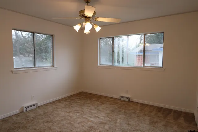 an empty room with a chandelier fan and windows