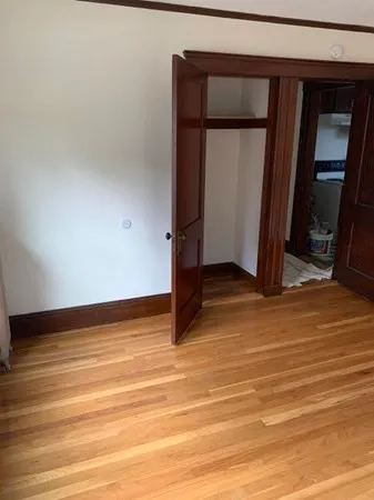 a view of an empty room with wooden floor and a mirror