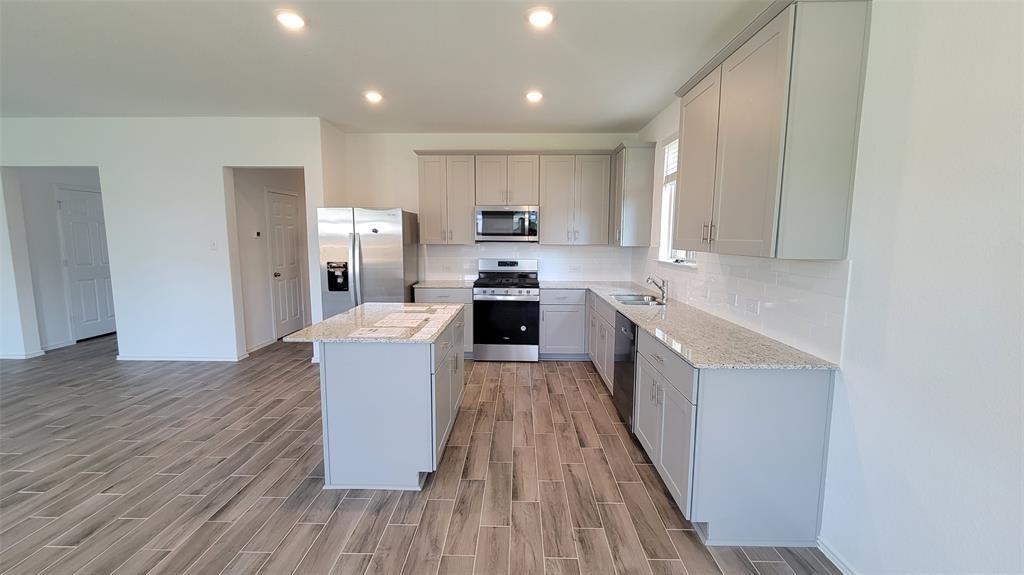452 Pickrell Loop Georgetown, TX 78628 - Photo 4 of 19 Kitchen featuring stainless steel appliances, wood tiled floors, backsplash, a kitchen island, and light stone counters